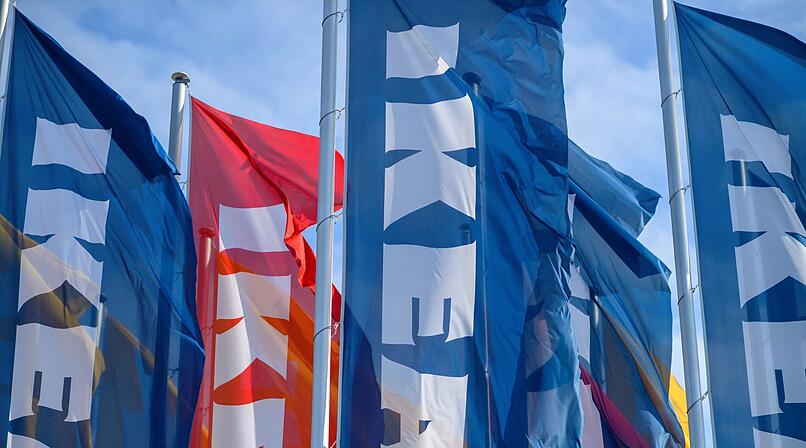 Blau-rote Fahnen mit Ikea-Logo wehen im Wind vor blauem Himmel. Sie symbolisieren die Ankunft eines neuen Möbelhauses nahe Bamberg.