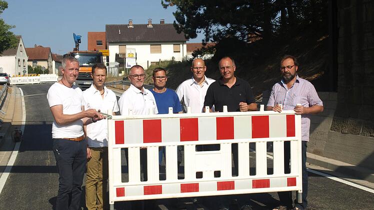 Fachingenieur Bernhard Klauer, Matthias Wacker und Joachim Dietz als Verantwortliche vom Staatlichen Bauamt Schweinfurt sowie stellvertretender Bürgermeister Gerhard Fischer (3. von links) zusammen mit Mitarbeitern der Firma Hell entfernen das Sperrschild von der Fahrbahn.