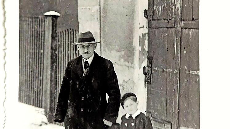 Die Fotografie von etwa 1949 zeigt Albert Schloß vor seinem Wohnhaus in Mühlhausen, zusammen mit dem etwa sechsjährigen Ralf Kriegel, dem Enkel von Frau Preussner, die eine Freundin der Eheleute Schloß gewesen ist.