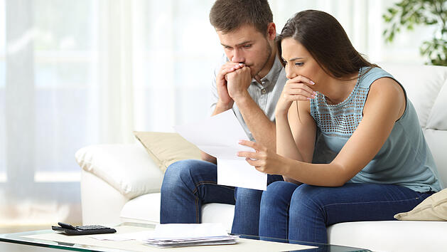 Mann und Frau sitzen auf Sofa und lesen einen Brief.