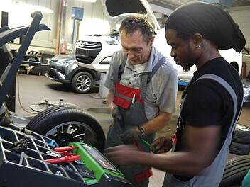 Edgar Luthardt erkl&auml;rt Hilfsarbeiter Chucks Smith das Arbeiten an der Wuchtmaschine. Smith beginnt im September eine Ausbildung zum Kfz-Mechatroniker. Foto: Rebecca Vogt