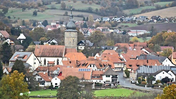 Blick auf Pfarrweisach mit der Pfarrkirche St. Kilian in der Mitte. Im Hintergrund lugen die Häuser von Junkersdorf hervor, eingebettet in baum- und heckenreiche Höhenzüge.