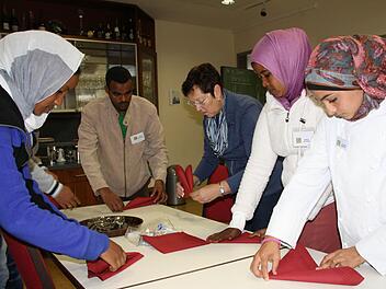 Mehr als Servietten-Falten: Wenn Fachlehrerin Gabi Steige (Mitte) mit Asylbewerbern den Tisch deckt, geht es vor allem um das Erlernen der Sprache und um Orientierungshilfe. Leider ist die neue Klasse der Berufsschule ein zu seltenes Angebot, in vielen Orten springen Ehrenamtliche in die Bresche. Foto: Ralf Ruppert