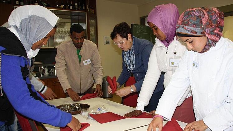 Mehr als Servietten-Falten: Wenn Fachlehrerin Gabi Steige (Mitte) mit Asylbewerbern den Tisch deckt, geht es vor allem um das Erlernen der Sprache und um Orientierungshilfe. Leider ist die neue Klasse der Berufsschule ein zu seltenes Angebot, in vielen Orten springen Ehrenamtliche in die Bresche. Foto: Ralf Ruppert