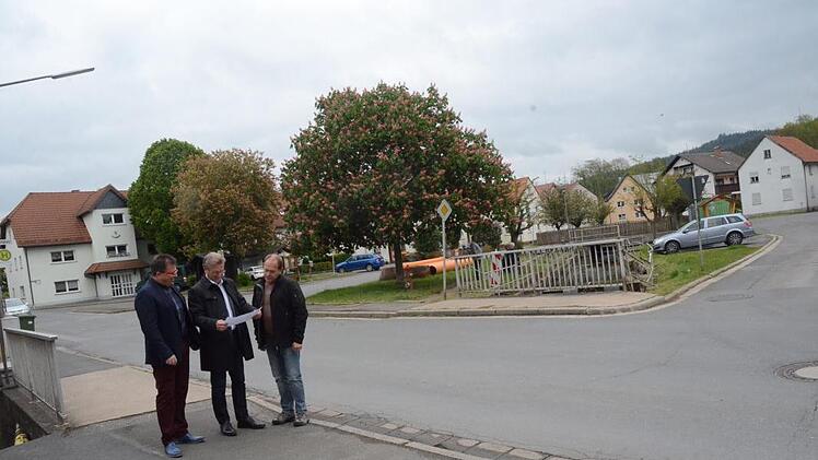 Bürgermeister Rainer Detsch (Mitte) und Geschäftsleiter Rainer Förtsch (links) mit Bauhofleiter Günter Hempfling zeigen den Kernpunkt der Arbeiten in der Ortsmitte, die ab Dienstag kommender Woche zu einer Vollsperrung der Ortsdurchfahrt in Reitsch führen werden. Die Brücke vorne wird vollständig erneuert, die Straße rechts wird in der Ein- und Ausfahrt verbreitert. Foto: K.- H. Hofmann