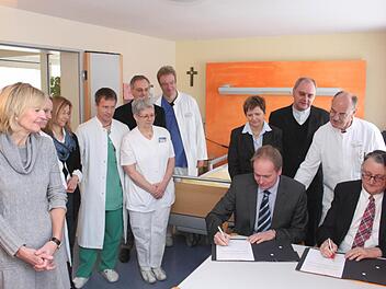Landrat Eberhard Irlinger (vorne rechts) und Caritas-Geschäftsführer Markus Beck (daneben) unterzeichneten in einem Zimmer der Palliativstation des Höchstadter Krankenhauses den Kooperationsvertrag. Im Hintergrund alle, die auf dieser Station aktiv sind.