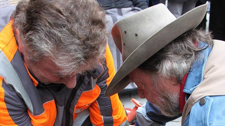 Ein Arbeiter assistiert dem Künstler Gunter Demnig (r.) beim Herausheben eines Pflastersteins, um dort die Gedenksteine platzieren zu können.
