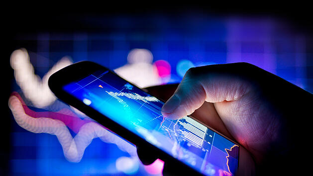 Eine Person, die mit ihrem Handy Aktienkurse in Echtzeit verfolgt A person using a mobile phone to track real time stocks and shares data mobile global business