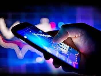 Eine Person, die mit ihrem Handy Aktienkurse in Echtzeit verfolgt A person using a mobile phone to track real time stocks and shares data mobile global business