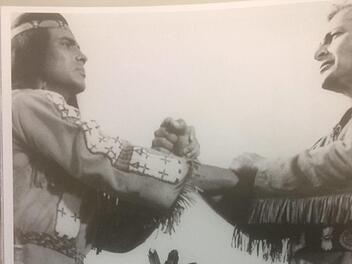 In "Winnetou 1" werden Häuptling Winnetou (Pierre Brice) und Old Shatterhand (Lex Barker) zu Blutsbrüdern, beobachtet von Winnetous Vater Intschu-tschuna (Mavid Propovic)  und Schwester Nscho-tschi (Marie Versini)Karl-May-Verlag