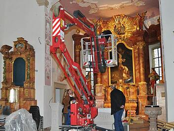 Mit einer Hebebühne gelangt der Elektriker im Chorbogen leicht an die Lichtleisten. Pfarrer Kosma Rejmer (links) am Altar und Rolf Drux (rechts) beobachten die Arbeiten gespannt. Foto: Ingrid Kohles