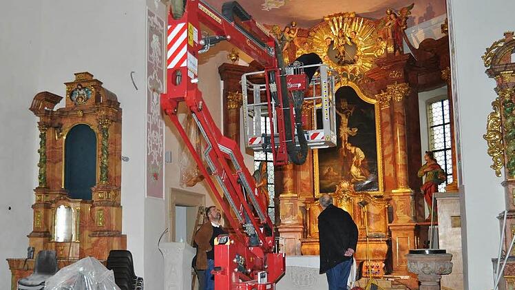 Mit einer Hebebühne gelangt der Elektriker im Chorbogen leicht an die Lichtleisten. Pfarrer Kosma Rejmer (links) am Altar und Rolf Drux (rechts) beobachten die Arbeiten gespannt. Foto: Ingrid Kohles