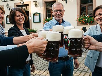 Ein paar Frauen und Männer mittleren Alters stoßen vor einer Brauereigaststätte mit Krügen an, in denen Bockbier ist.