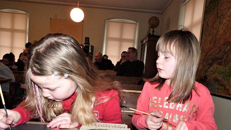 Mira und Hannah versuchen, mit dem Schiefergriffel auf der Tafel zu schreiben.