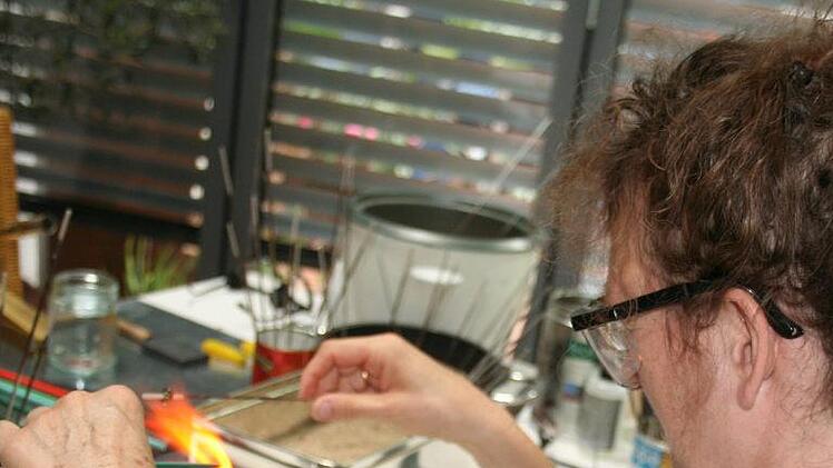 Geschlossene Jalousien machen nicht nur das Arbeiten angenehmer, wenn bei tropischen Temperaturen Glas mit dem Bunsenbrenner geschmolzen wird. Im Dämmerlicht kann man auch die Flamme besser sehen, verrät  Designerin Gisela Pröls-Beck, in deren Werkstatt der Kurs stattfand. Foto: vhs-Coburg