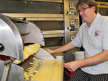 Jürgen Raab an der Baumkuchenmaschine, die noch sein Vater angeschafft hat. Der Backvorgang der Biskuit-Sand-Masse in dünnen Schichten auf dem Stab vor den glühend heißen Grillstäben erfordert viel Gespür für den richtigen Moment. Auch für den Lichtenfelser Konditormeister ist diese Spezialität etwas nicht Alltägliches. Foto: Ramona Popp