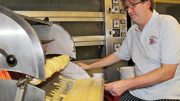 Jürgen Raab an der Baumkuchenmaschine, die noch sein Vater angeschafft hat. Der Backvorgang der Biskuit-Sand-Masse in dünnen Schichten auf dem Stab vor den glühend heißen Grillstäben erfordert viel Gespür für den richtigen Moment. Auch für den Lichtenfelser Konditormeister ist diese Spezialität etwas nicht Alltägliches. Foto: Ramona Popp