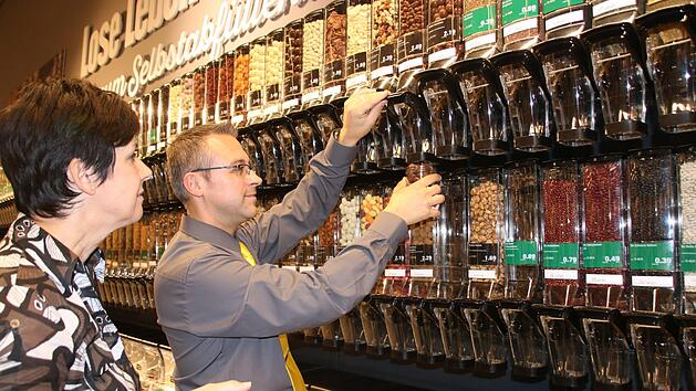 Marktinhaber Michael Seidl f&uuml;llt f&uuml;r Kundin Silke Ludwig ein Glas mit Pecan-Schokon&uuml;ssen ab. Seit Mittwoch gibt es im Edeka eine neue Abteilung mit Unverpackt-Lebensmitteln. Die Palette reicht von Getreideflocken &uuml;ber S&uuml;&szlig;waren bis hin zu Nudeln, Kaffee und Essig. Foto: Jochen N&uuml;tzel