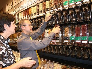 Marktinhaber Michael Seidl füllt für Kundin Silke Ludwig ein Glas mit Pecan-Schokonüssen ab. Seit Mittwoch gibt es im Edeka eine neue Abteilung mit Unverpackt-Lebensmitteln. Die Palette reicht von Getreideflocken über Süßwaren bis hin zu Nudeln, Kaffee und Essig. Foto: Jochen Nützel