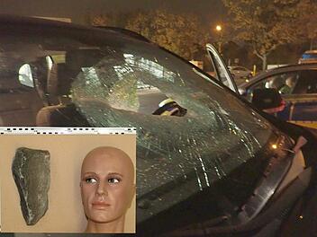 Die Bildkombo zeigt die durchschlagene Windschutzscheibe eines Autofahrers auf der A42. Das kleinere Bild zeigt, wie gro&szlig; der Stein ist, der auf das Fahrzeug geworfen wurde. Fotos: Polizei