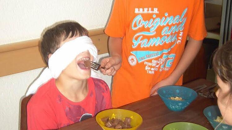 Leon (rechts) "füttert" Yannik, dessen Augen mit einem Tuch verbunden wurden, mit verschiedenen Köstlichkeiten. Yannik muss erraten, um was es sich dabei handelt.