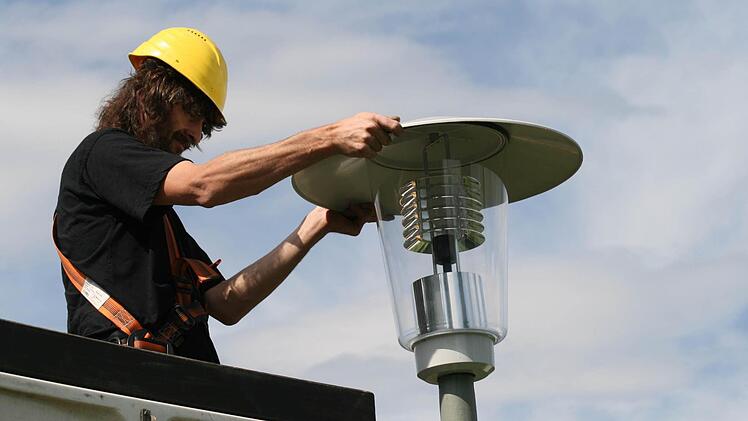 Ein Arbeiter wechselt einen Leuchtkopf einer Straßenlampe aus. Foto: Archiv/Jürger Gärtner