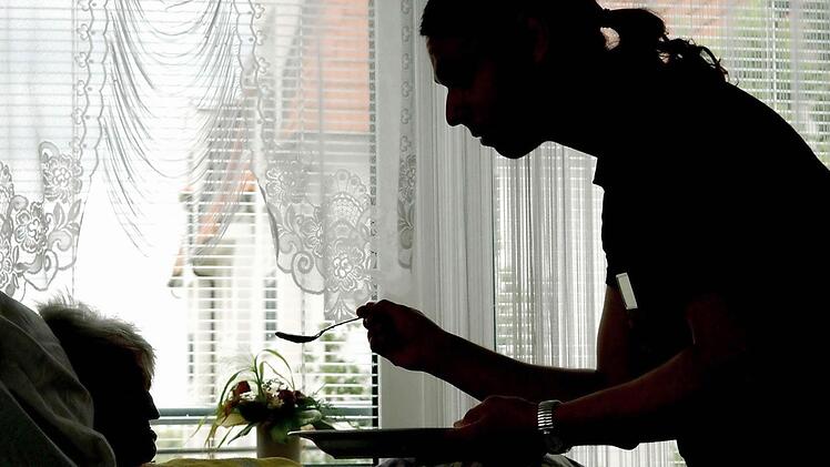 In einem Seniorenzentrum in Frankfurt (Oder) - hier eine Archivaufnahme aus dem Jahr 2004 -  füttert ein Pfleger eine Heimbewohnerin, die im Bett liegt.  Foto: Patrick Pleul/dpa/Archiv