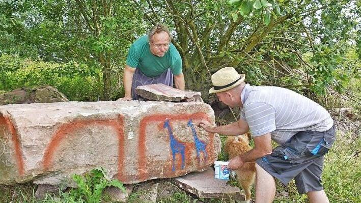 Klaus Langmann an seinem "Altarstein". Wie die Steinzeitmenschen zeichnet er mit dem Pinsel zwei Giraffen auf den Stein. Sein Kollege Gernot Ehrsam betrachtet das Kunstwerk von oben.  Foto: Friedrich