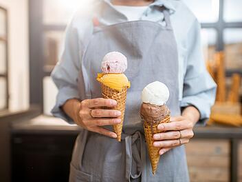 Eis, Speiseeis, Eiscreme, Female seller holding two yummy ice creams in waffle cone at the shop, close-up Verk&auml;uferin h&auml;lt zwei leckere Eissorten in einer Waffelt&uuml;te im Laden, Nahaufnahme