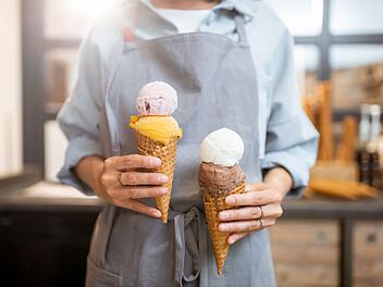 Eis, Speiseeis, Eiscreme, Female seller holding two yummy ice creams in waffle cone at the shop, close-up Verk&auml;uferin h&auml;lt zwei leckere Eissorten in einer Waffelt&uuml;te im Laden, Nahaufnahme
