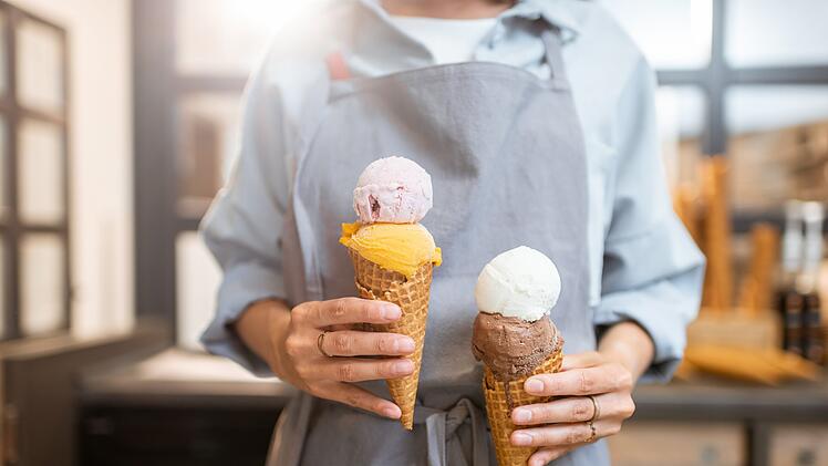 Eis, Speiseeis, Eiscreme, Female seller holding two yummy ice creams in waffle cone at the shop, close-up Verkäuferin hält zwei leckere Eissorten in einer Waffeltüte im Laden, Nahaufnahme