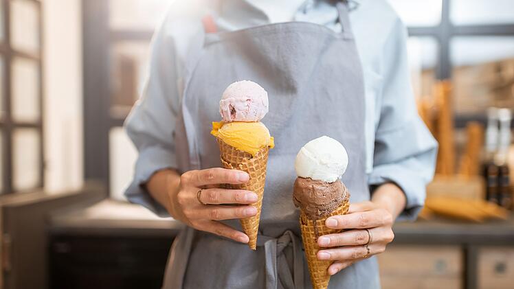 Eis, Speiseeis, Eiscreme, Female seller holding two yummy ice creams in waffle cone at the shop, close-up Verk&auml;uferin h&auml;lt zwei leckere Eissorten in einer Waffelt&uuml;te im Laden, Nahaufnahme