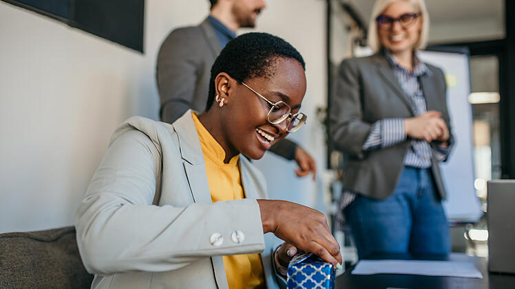 The team celebrated a female colleague's birthday in the office during a meeting. Focus on a black businesswoman opening a gift