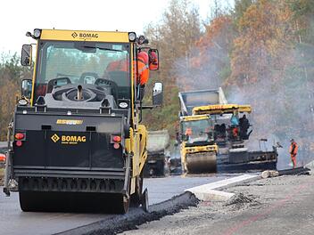 Der heiße Asphalt (hinten) dampft noch, während eine Maschine (im Vordergrund) bereits die Kanten glättet. Nach zwei Tagen sind die Asphaltierungsarbeiten an der Strecke zwischen Ibind und der B303 weit fortgeschritten. Foto: Eckehard Kiesewetter