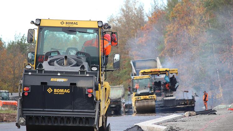 Der heiße Asphalt (hinten) dampft noch, während eine Maschine (im Vordergrund) bereits die Kanten glättet. Nach zwei Tagen sind die Asphaltierungsarbeiten an der Strecke zwischen Ibind und der B303 weit fortgeschritten. Foto: Eckehard Kiesewetter