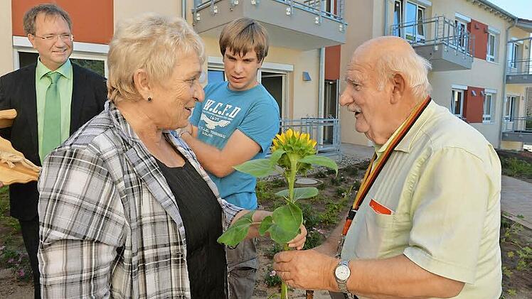 Mit Ernst Hofmann (rechts ) hält die Stimmung Einzug im neuen AWO-Serniorenzentrum. Zur Begrüßung gibt's eine Sonnenblume von Fachbereichsleiterin Gundi Heusinger. Geschäftsführer Werner Dippold (links)begrüßt die ersten Bewohner persönlich. Foto: Ronald Rinklef