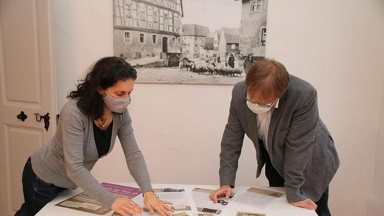 Christine Schikora und Ortwin Guhling betrachten im Heimatspielhaus die Entwürfe der Schautafeln und die alten Ansichtskarten. Vom 17. Oktober bis zum 8. November ist die Ausstellung über 235 Jahre Münnerstädter Postgeschichte zu sehen. Foto: Thomas Malz