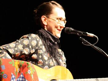 Mit ihren zurückgeflochtenen Haaren und ihrer Gitarre sitzt Martina Schwarzmann bei ihrem Gastspiel im Kreiskulturraum auf dem roten Stuhl. Sie behauptet von sich, dass sie privat sehr unauffällig und ihr Körper der "Wahnsinn" sei. Foto: Michael Wunder