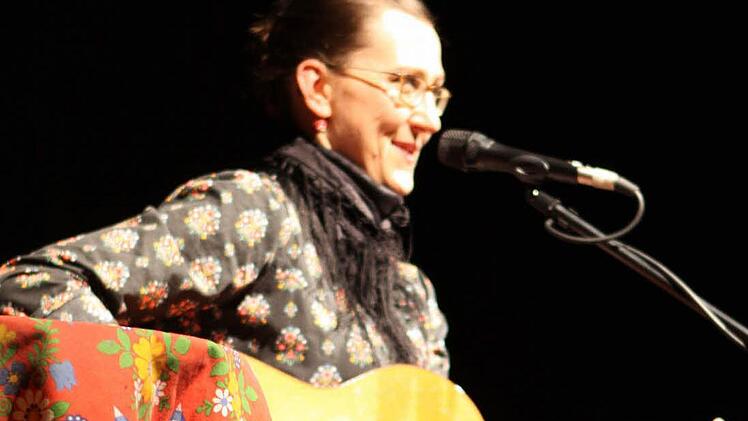 Mit ihren zurückgeflochtenen Haaren und ihrer Gitarre sitzt Martina Schwarzmann bei ihrem Gastspiel im Kreiskulturraum auf dem roten Stuhl. Sie behauptet von sich, dass sie privat sehr unauffällig und ihr Körper der "Wahnsinn" sei. Foto: Michael Wunder