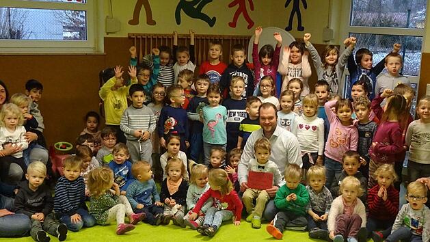 Sebastian Wirth sitzt mitten in den Kindern, die sich schon sehr auf ihren neuen Spielplatz freuen. Wirths Sohn sitzt auf seinem Schoß, er hält den Scheck über 500 Euro in der Hand. Foto: Gabriel Raab