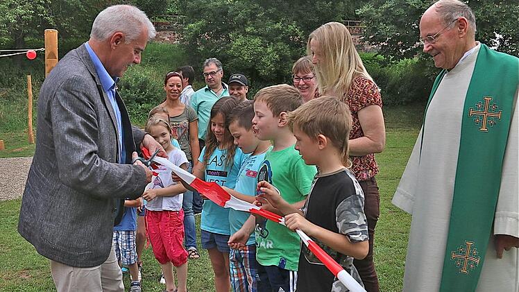Bürgermeister Jürgen Karle durchschneidet symbolisch das Absperrband des neugestalteten Spielplatzes. Die Mädchen und Jungen warten schon ganz ungeduldig. Foto: Gerd Schaar