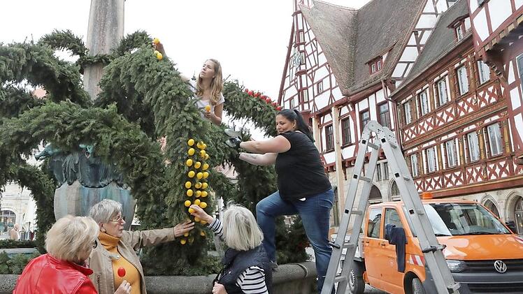 Während von unten die Gästeführerinnen Marlene Hahn, Ingeborg Oelschner und Ulli Baier (v.l.) Regieanweisungen geben, stecken die Gartenamtsmitarbeiterinnen Anke Schönbrodt (r.) und Eva Giesel (oben) von der Leiter aus die rot-gelben Eier an den Osterbrunnen.  Foto: Barbara Herbst