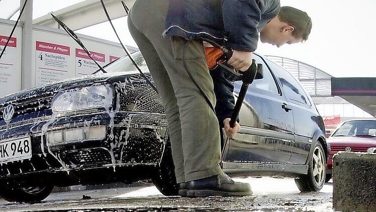 Ein Mann befreit sein Auto vom Winterschmutz. Foto: dpa