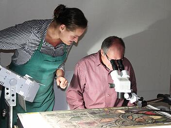 Pfarrer P. Markus Reis wagt einen Blick durchs Mikroskop. Martha Hör erläutert ihm das Schadensbild an dem Kirchenfenster. Fotos: Heike Beudert