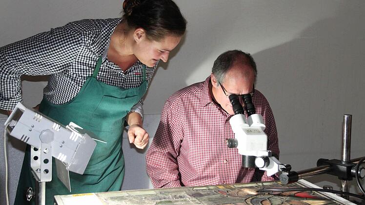 Pfarrer P. Markus Reis wagt einen Blick durchs Mikroskop. Martha Hör erläutert ihm das Schadensbild an dem Kirchenfenster. Fotos: Heike Beudert