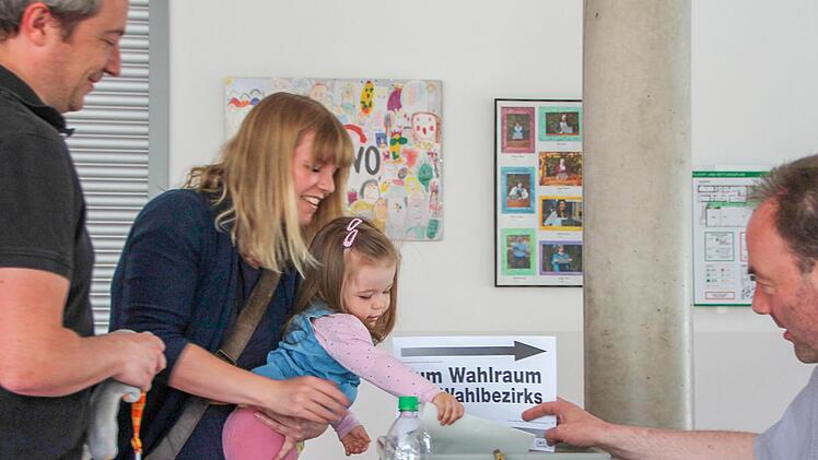 Früh übt sich, was ein Jungwähler werden will: Emily darf in Ebern die Stimmzettel ihrer Eltern Sonja und und Philipp Nacke einwerfen. Rechts: Wahlhelfer Bernhard Kaufmann zeigt den Schlitz in der Urne.