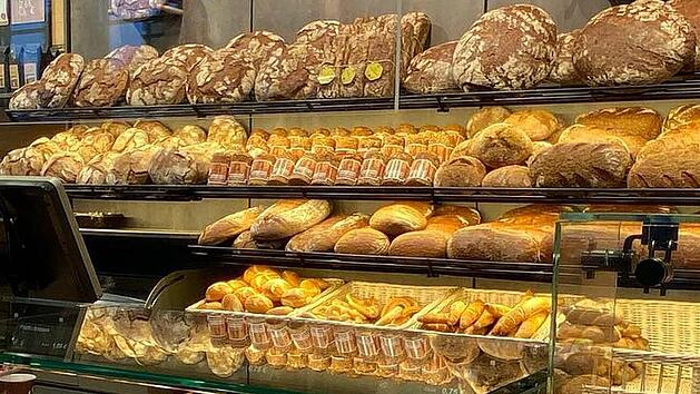 Ein Regal in einer B&auml;ckerei, gef&uuml;llt mit verschiedenen Brotsorten und Backwaren. Es zeigt eine Vielfalt an frisch gebackenen Produkten, m&ouml;glicherweise von preisgekr&ouml;nten B&auml;ckereien.