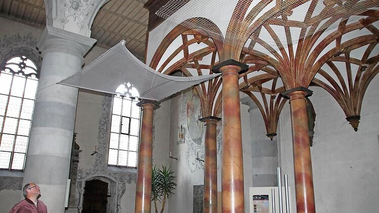 Stadtpfarrer Pater Markus begutachtet die beiden Netze, die derzeit zu Testzwecken in der Kirche hängen. Das grobmaschige, weniger auffällige Netz (rechts) soll demnächst im Kirchenschiff gespannt werden, damit kein lockerer Putz auf Kirchenbesucher fallen kann. Fotos: Heike Beudert