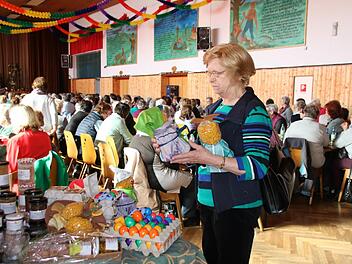 Irmgard Prietzel kommt schon viele Jahre zum Landfrauentag in die Rhönfesthalle Stangenroth. Hier steht sie am Verkaufsstand des Ramsthaler Bauernladens, an dem regionale Produkte angeboten werden. Im Hintergrund sind die voll bestetzten Tische erkennbar. Foto: Kathrin Kupka-Hahn