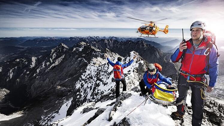 Auch die zweite Staffel der "Bergretter im Einsatz" (ARD / BR)zeigt Bergwachteins&auml;tze in den bayerischen Alpen - hautnah und in beeindruckenden Bildern. Drei Angeh&ouml;rige der Bergwacht, die sich mit einer geretteten Person auf einem Berggipfel befinden, weisen einen anfliegenden Hubschrauber ein.